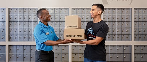 The UPS Store associate assisting a customer with packages in front of mailboxes.